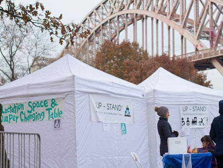 A woman in a hat stands in front of two outdoor tents and a sign that reads, "Lactation Space and Diaper Changing Table"