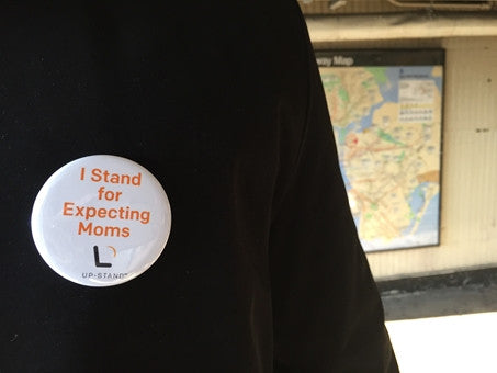A pin that reads "I stand for expecting moms" on a coat, in front of an NYC subway map