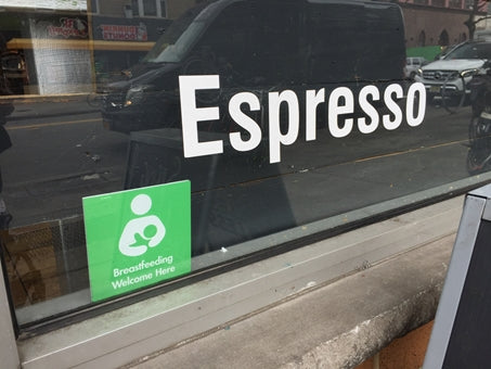 A green Breastfeeding Welcome Here sign in the window of a coffee shop